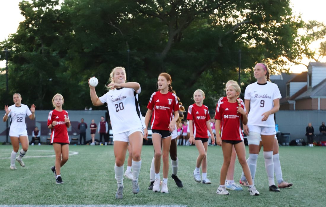 Olivia Anderson throws a signed ball into the stands pre-game, surrounded by a local youth soccer team. (Ashley Wilson | The Phoenix)